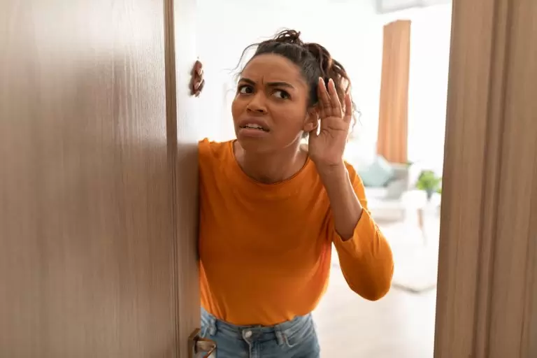 Displeased Black Lady Listening Standing In Opened Door At Home