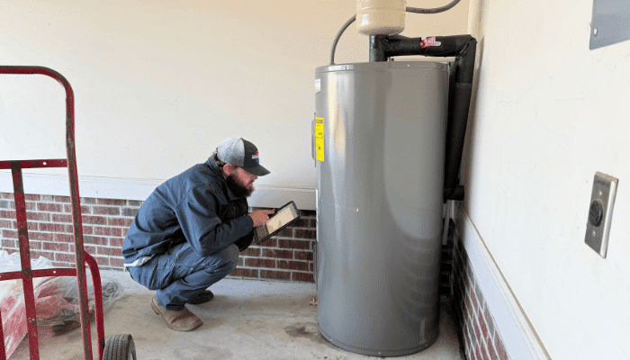 Technician inspecting a residential water heater in a garage during a service appointment.